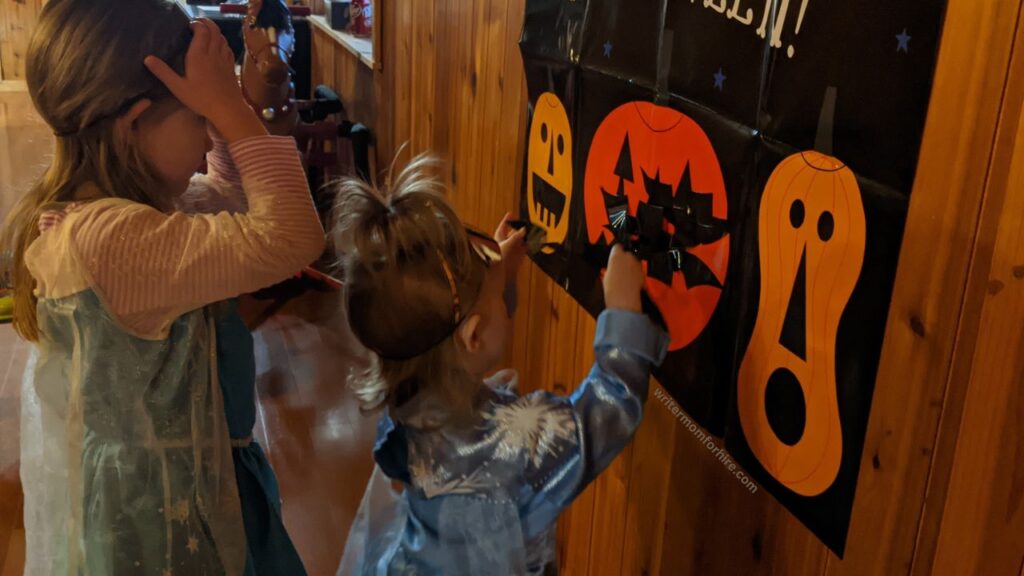 my daughters pinning faces onto jack-o-lanterns, both dressed as elsa from frozen